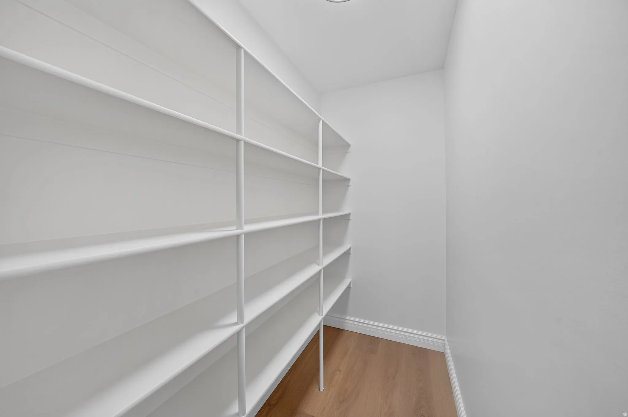 Walk-in pantry featuring extensive white shelving, recessed lighting, and wood-finish flooring