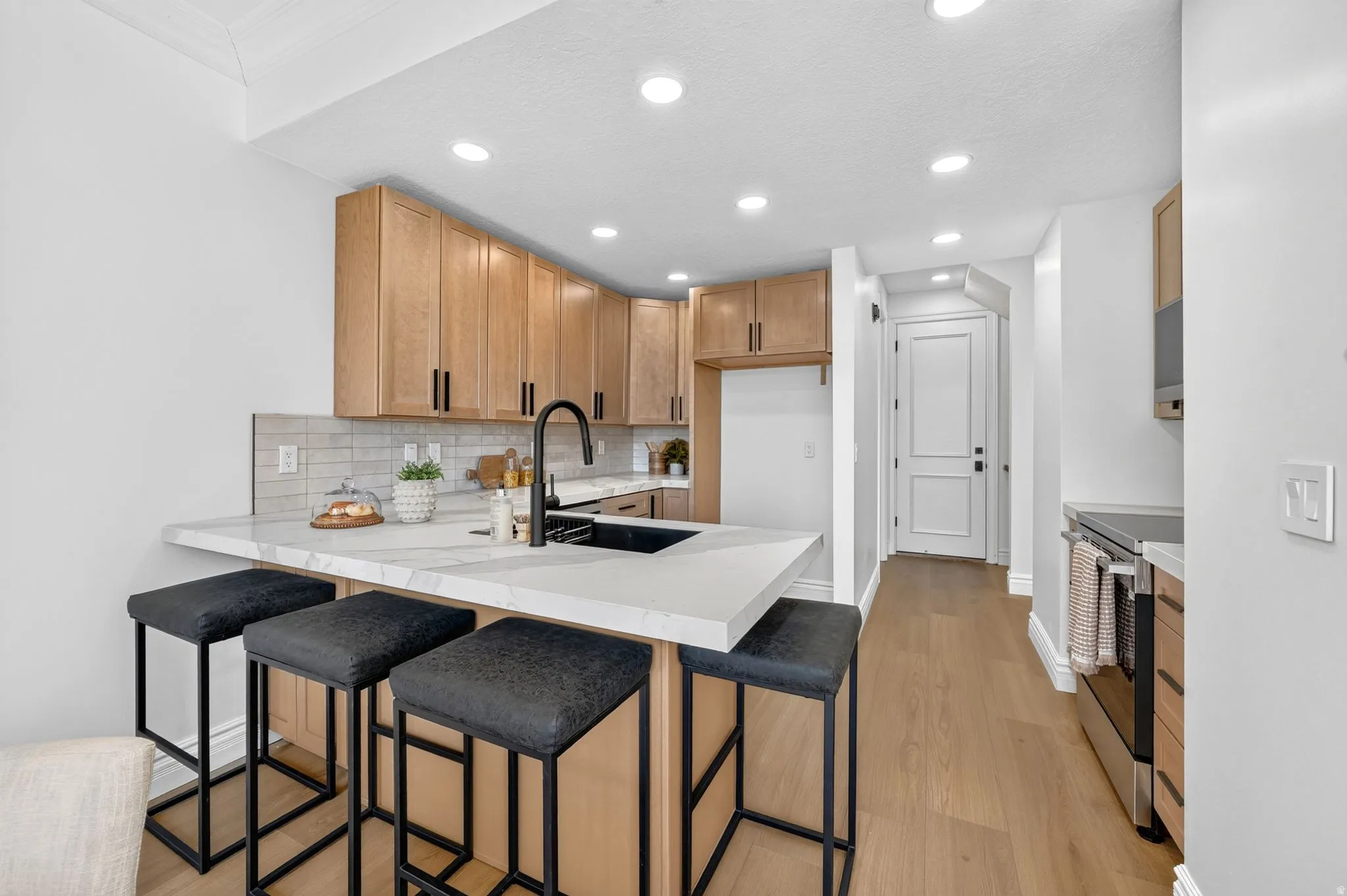 Kitchen featuring wood-finish cabinetry, light-toned countertops, a black sink with a matte black faucet, and stainless steel appliances