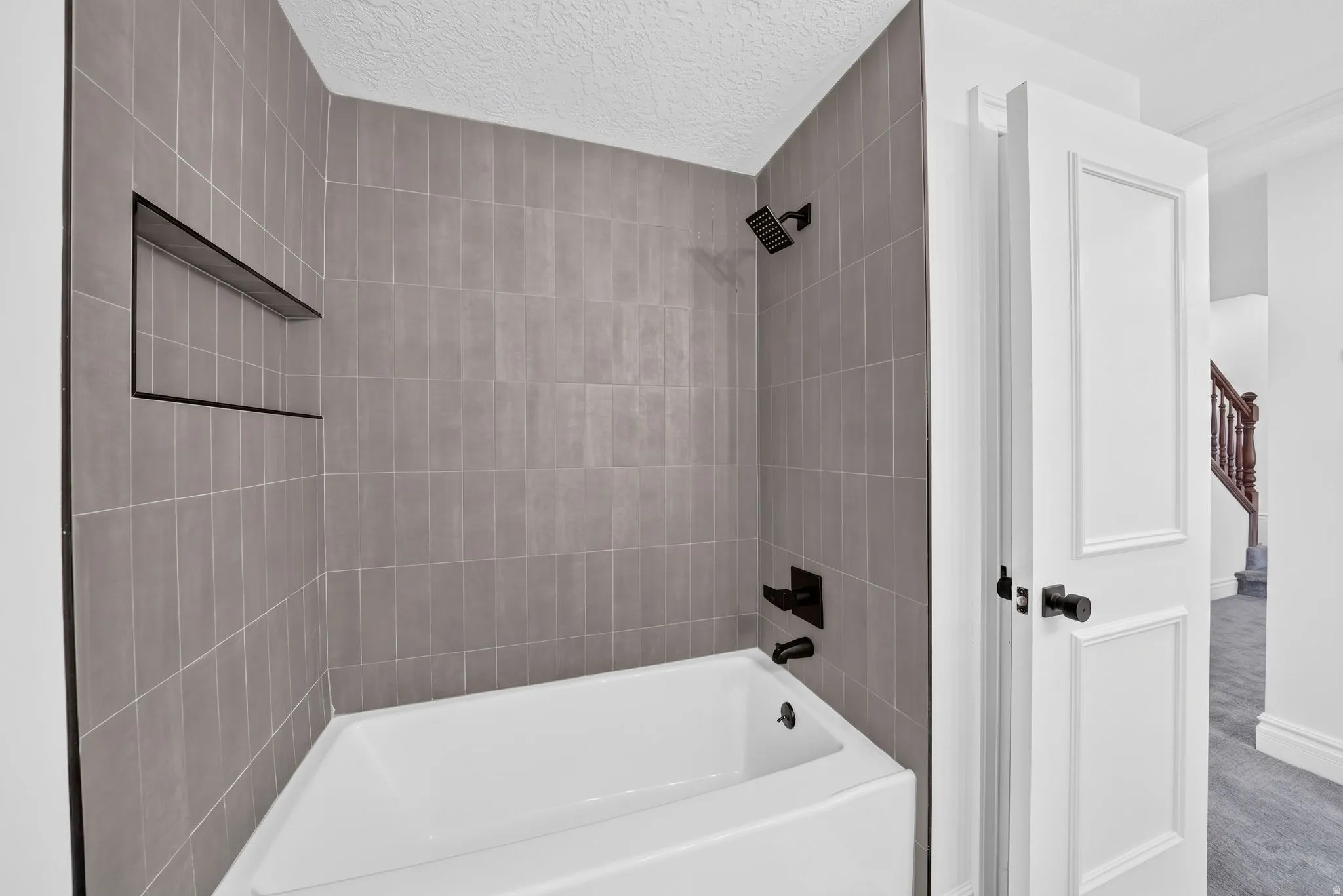 Bathtub with matte gray vertical tile surround, integrated shower niche, and matte black fixtures