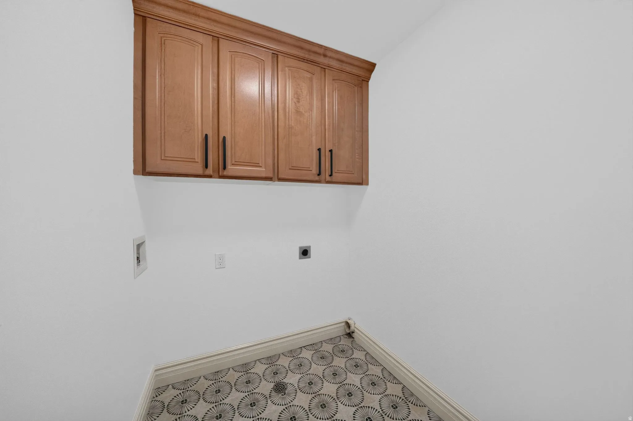 Built-in cabinetry with wood-finish doors and matte black hardware, white walls, patterned tile flooring with dark grout, and white baseboards