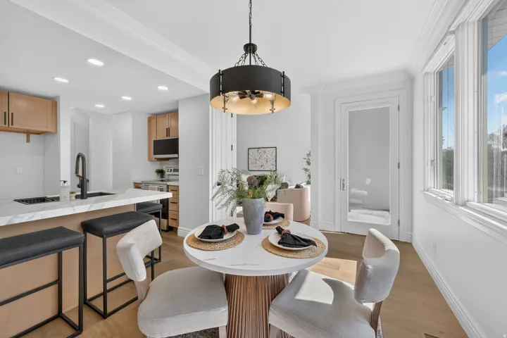 Open-concept dining area featuring a contemporary pendant light fixture, wood-finish flooring, and crown molding