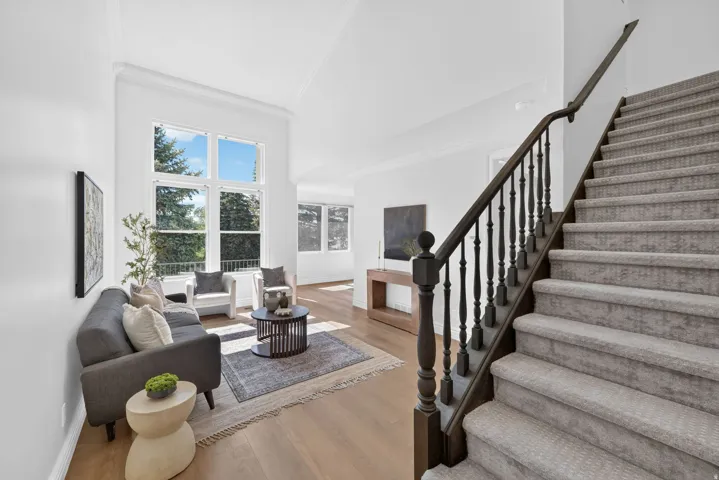 Two-story living area featuring tall windows, light wood-finish flooring, white walls, and crown molding