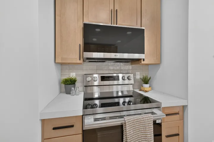 Kitchen featuring light wood-finish cabinetry, stainless steel oven and microwave, white countertops, and a gray tile backsplash