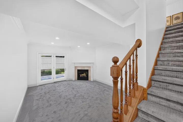 Spacious room featuring gray textured carpet, a fireplace with a stone mantel, and double glass-paneled doors