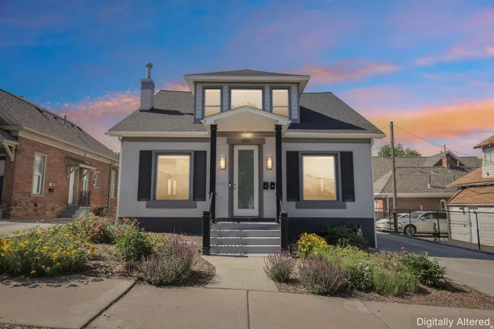 Traditional architecture featuring a light-colored exterior with contrasting dark trim and shutters, a prominent front porch with white columns, and a dormer window