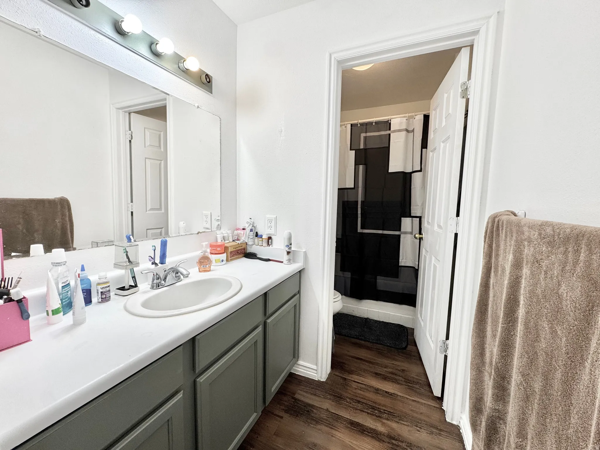 Bathroom vanity with a white countertop and oval undermount sink, illuminated by a strip light fixture above a large mirror