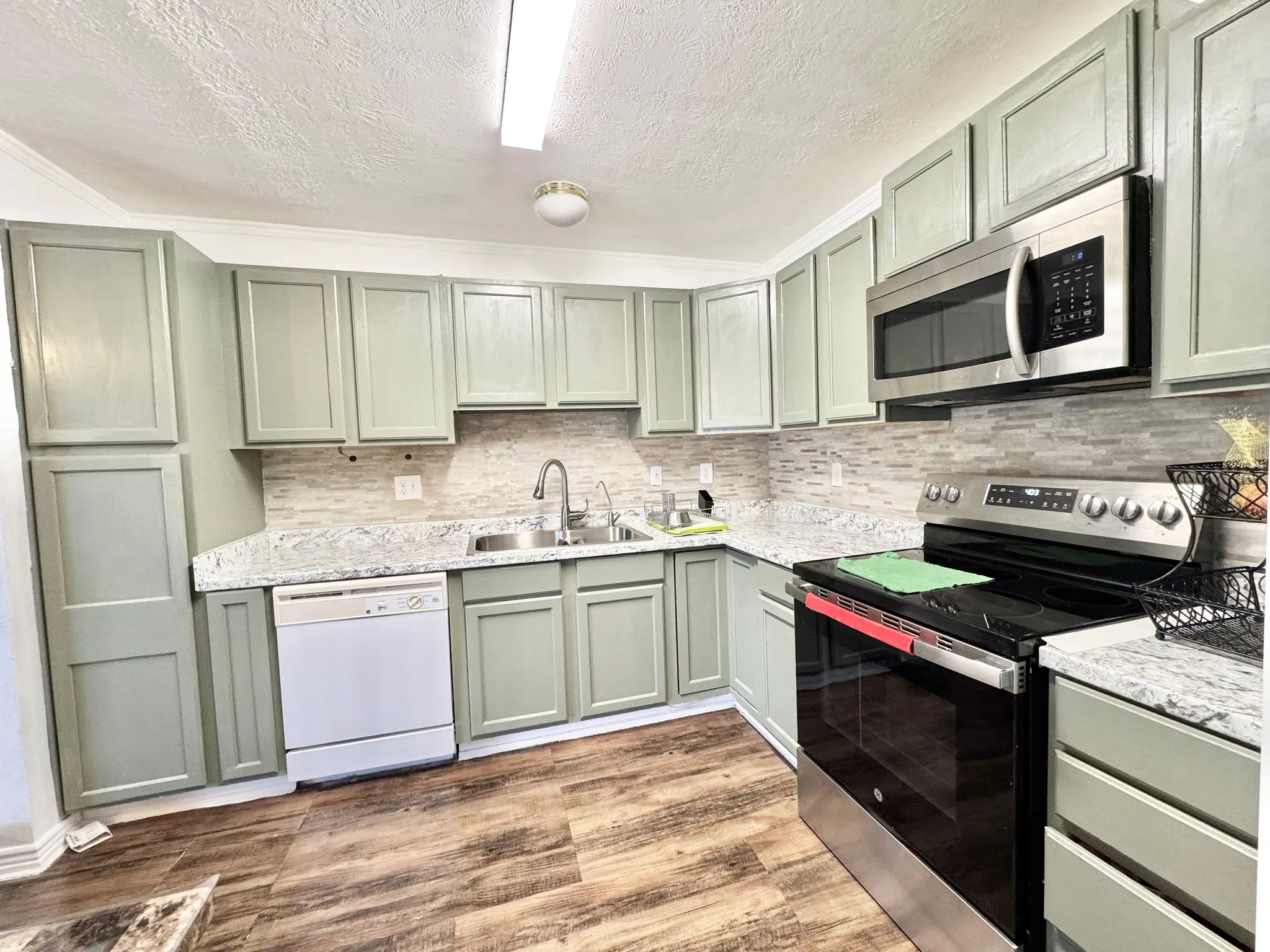 Kitchen featuring wood-finish flooring, light-colored cabinetry, stone-look countertops, a tile backsplash, and stainless steel appliances