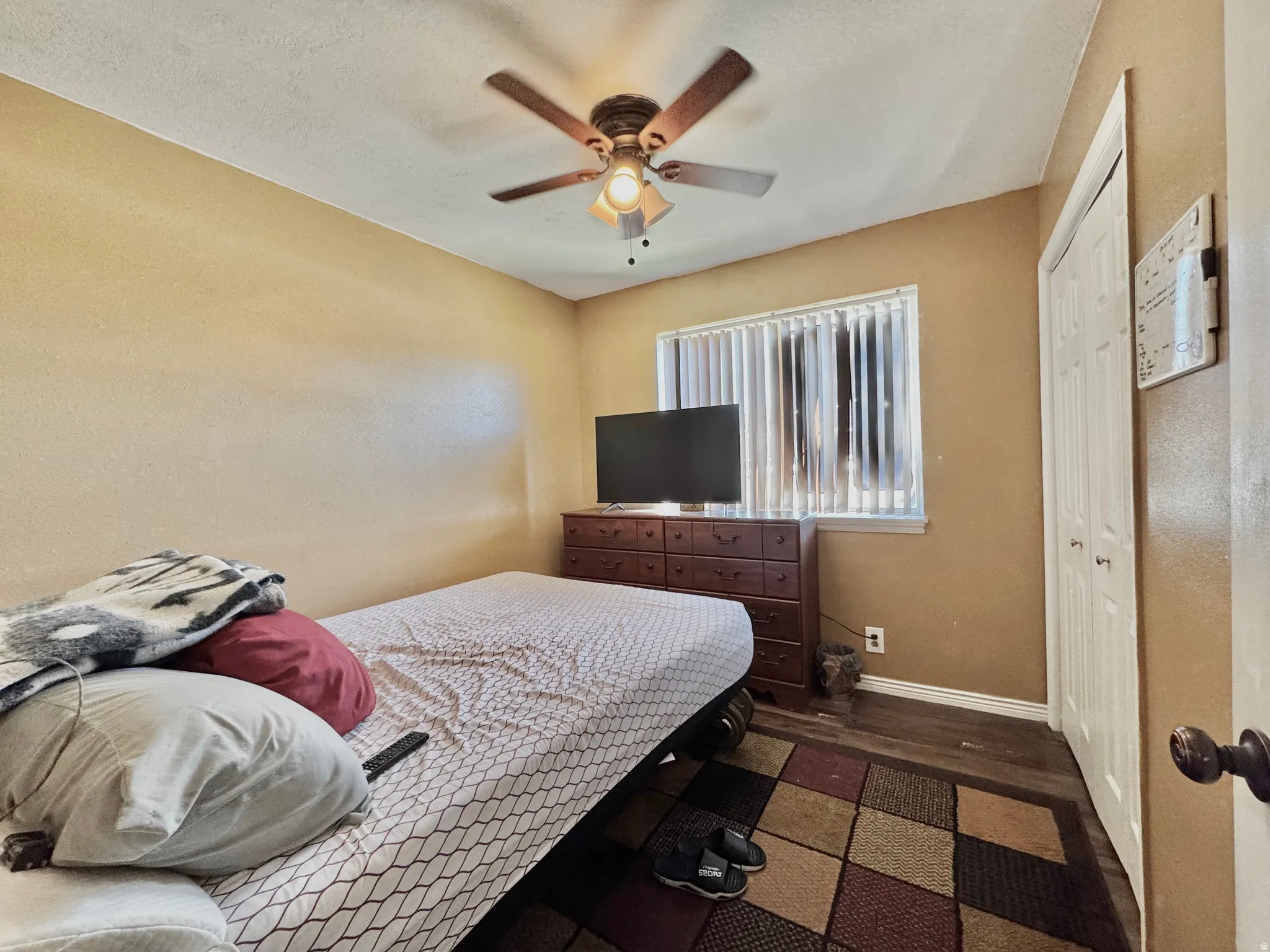 Room featuring wood-finish flooring, a ceiling fan with integrated lighting, and a window with vertical blinds