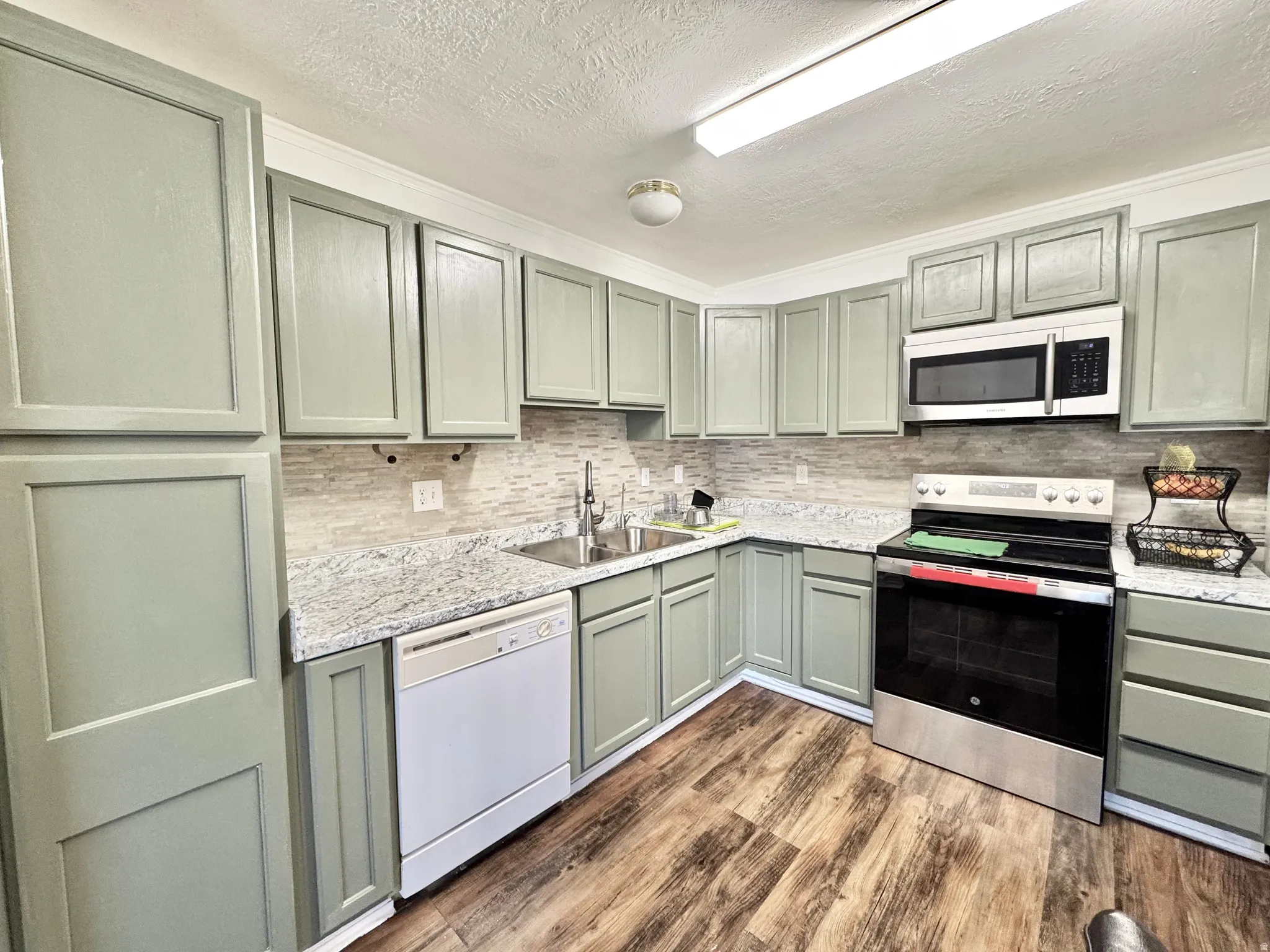 Kitchen featuring L-shaped cabinetry, wood-finish flooring, a tile backsplash, and light-toned countertops