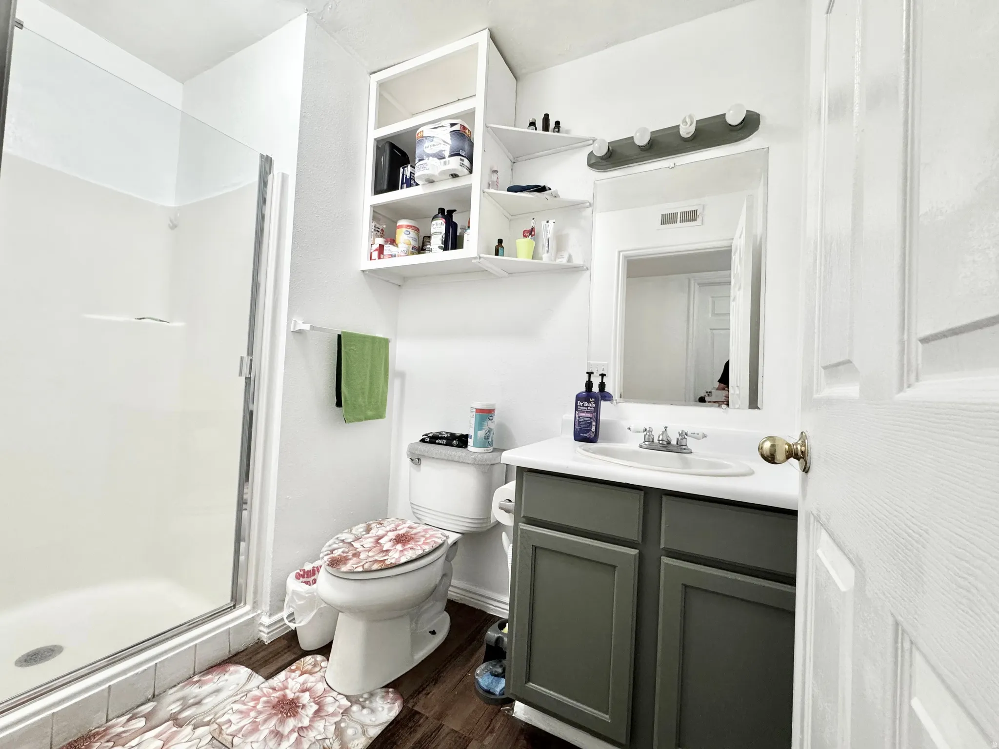 White bathroom featuring a glass-enclosed shower, white vanity with an integrated sink, dark gray cabinet base, and wood-finish flooring
