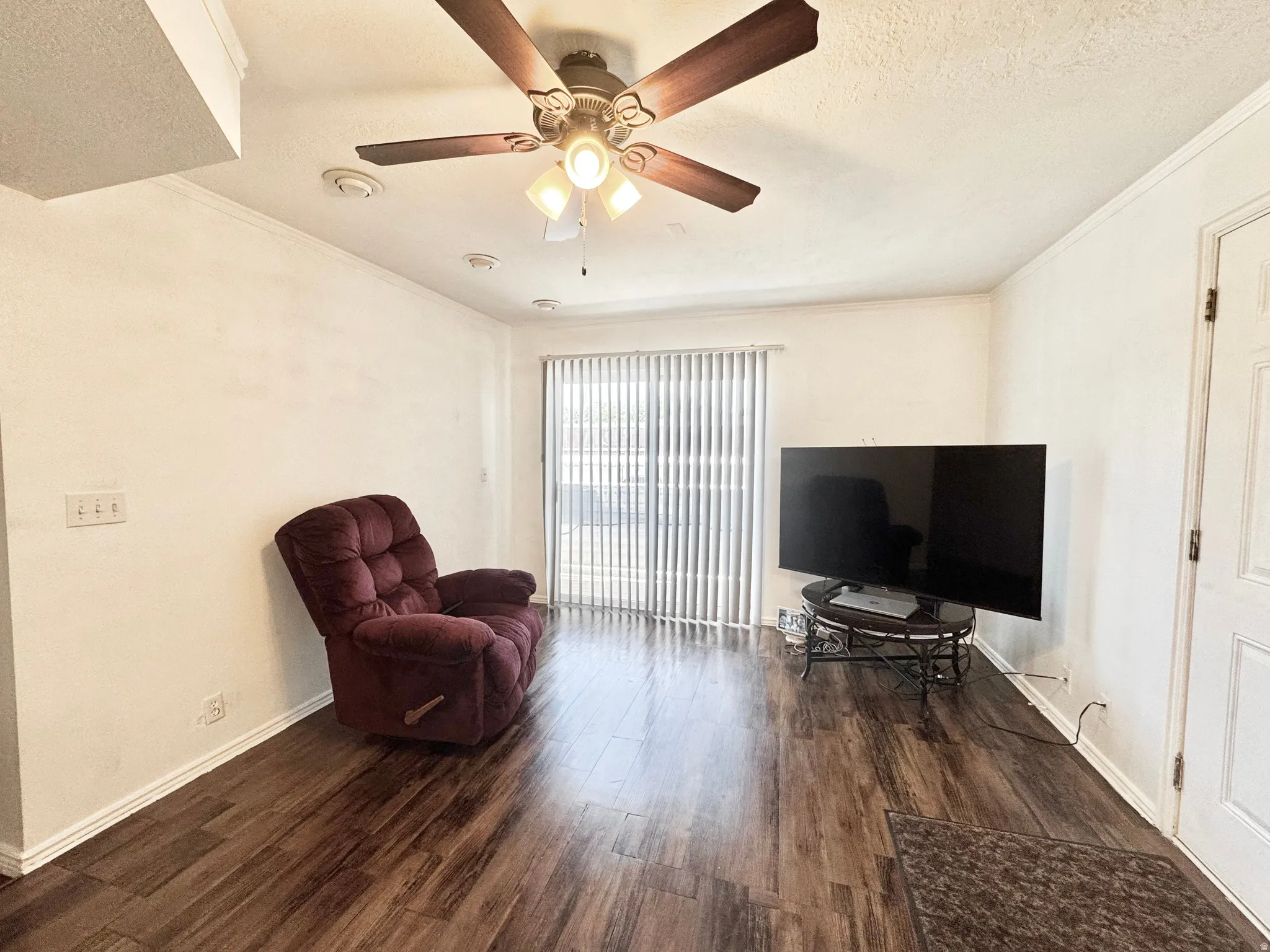 Spacious room featuring wood-finish flooring, white baseboards, and a ceiling fan with integrated lighting