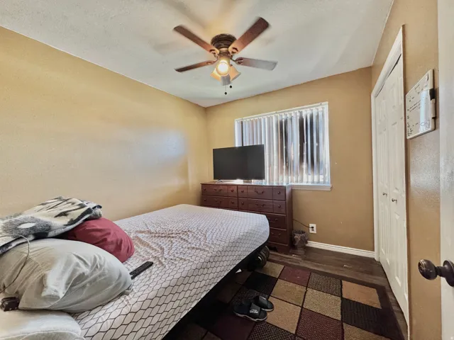 Room featuring wood-finish flooring, a ceiling fan with integrated lighting, and a window with vertical blinds