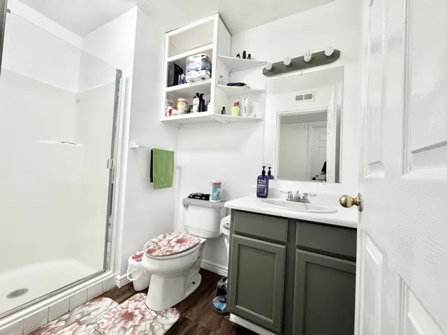 White bathroom featuring a glass-enclosed shower, white vanity with an integrated sink, dark gray cabinet base, and wood-finish flooring