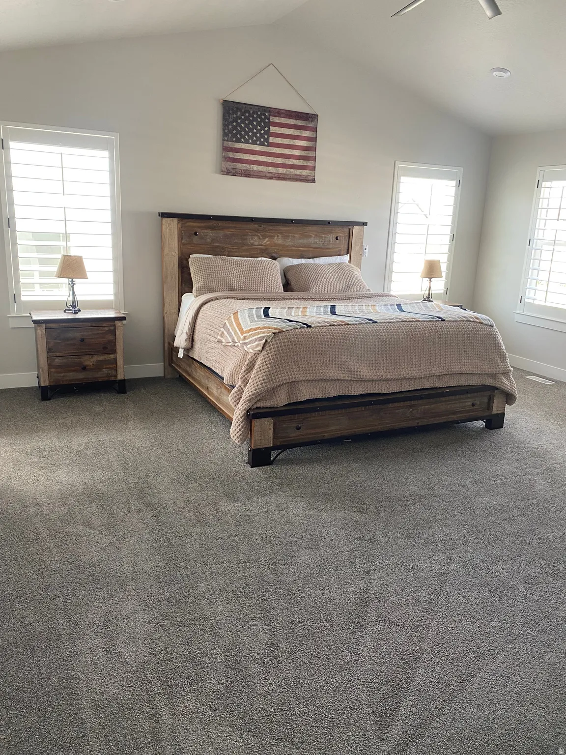 Spacious room featuring vaulted ceilings, plush carpeting, and dual windows with plantation shutters