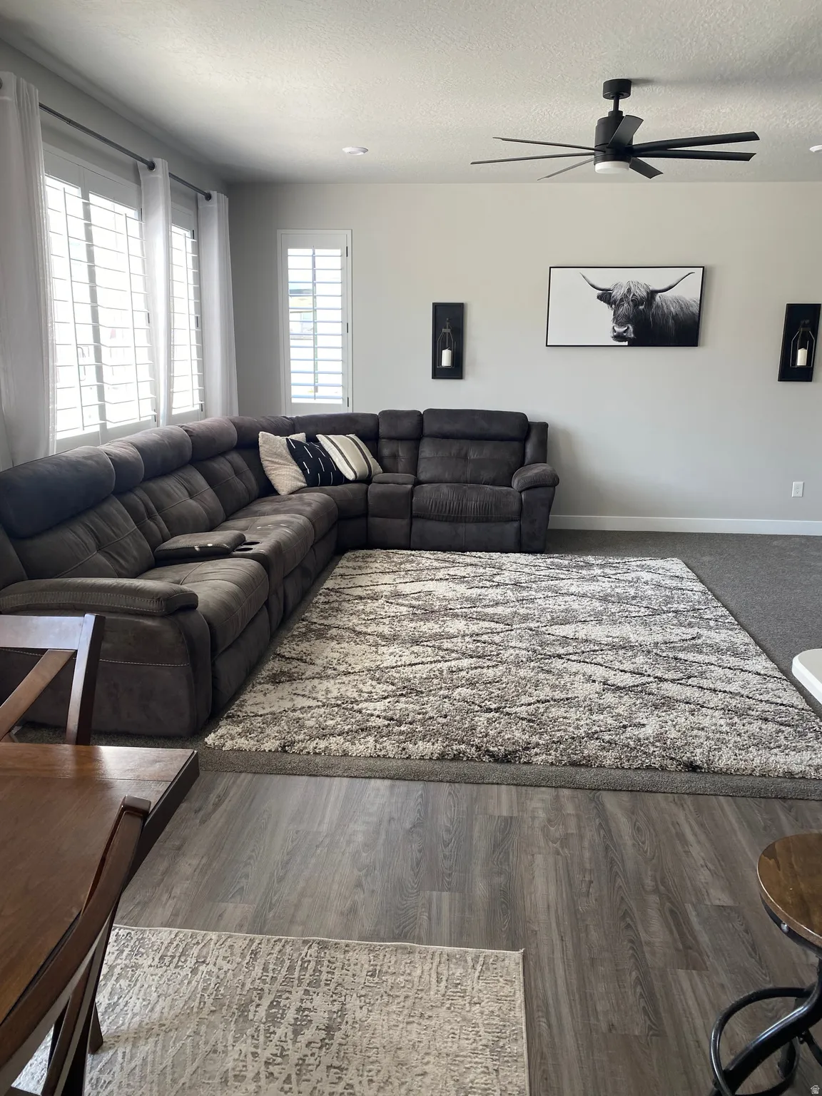 Living area featuring wood-finish flooring, a contemporary ceiling fan with integrated lighting, and multiple windows with plantation shutters