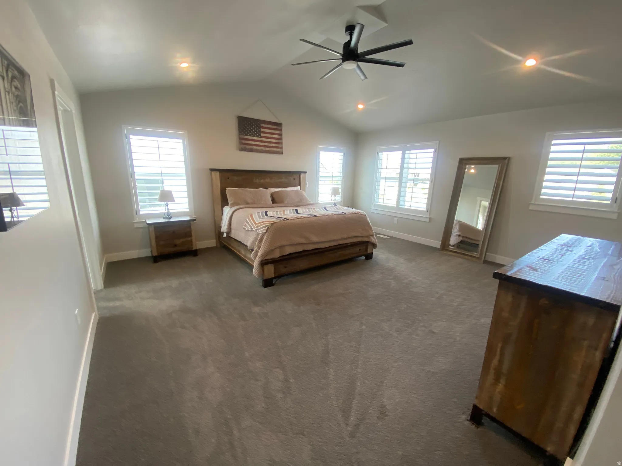 Carpeted room featuring a vaulted ceiling with a ceiling fan, recessed lighting, and multiple windows with plantation shutters