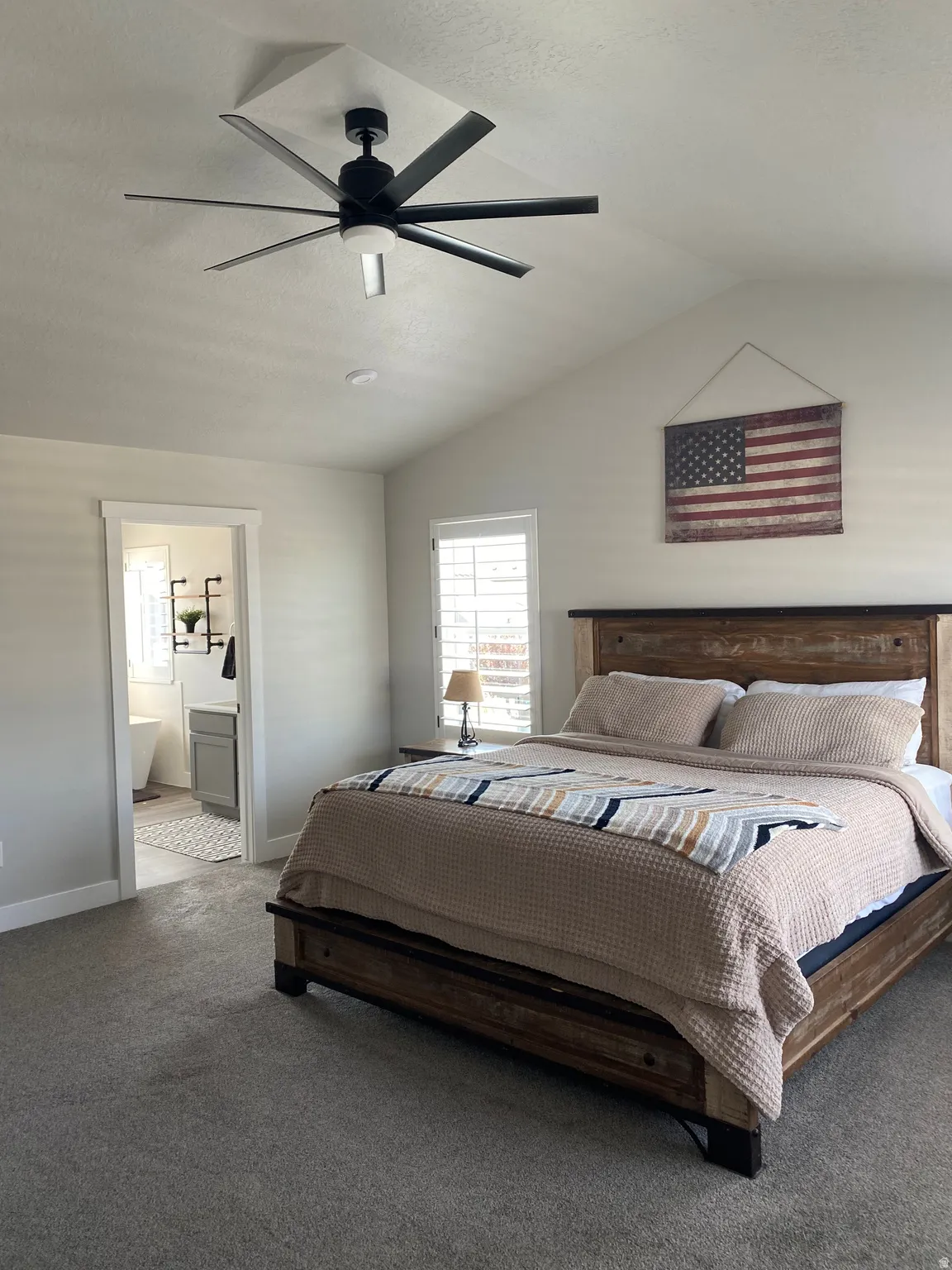 Vaulted ceiling bedroom featuring a modern black ceiling fan and soft gray carpeting
