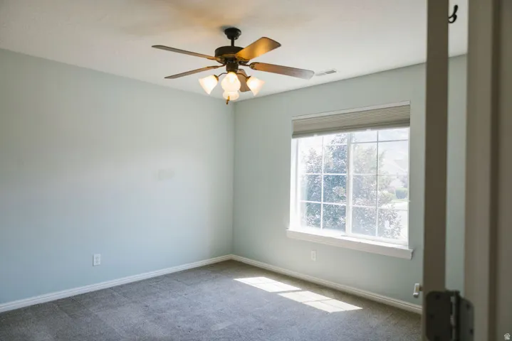 Carpeted room featuring a large window with horizontal blinds, a white window frame, and an overhead ceiling fan with integrated lighting