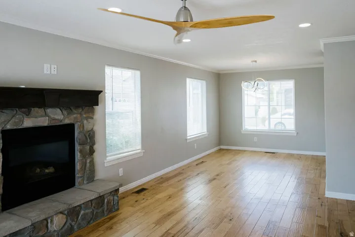 Living area featuring wood-finish flooring, a stone-faced fireplace with a dark wood mantel, and multiple windows