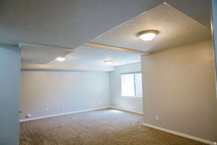 Spacious room featuring neutral wall tones, textured carpeting, and a window with blinds