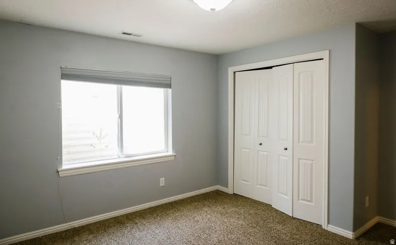 Carpeted room featuring a window with white trim, a closet with bi-fold doors, and a ceiling-mounted light fixture