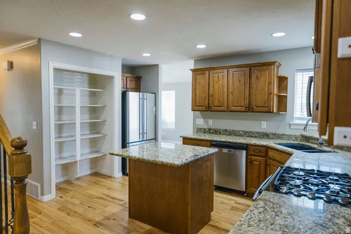 Kitchen featuring wood cabinetry, light-toned granite countertops, stainless steel appliances, and wood-finish flooring