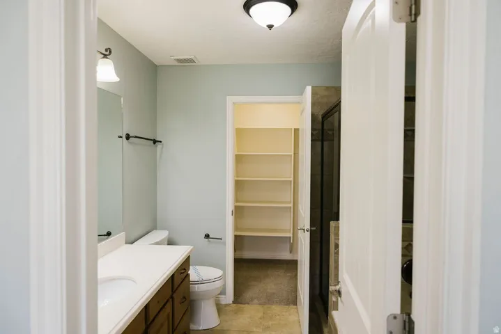 Bathroom featuring a single vanity with wood-finish cabinetry and a light-toned countertop, a toilet, and an adjacent walk-in shower with a framed glass enclosure