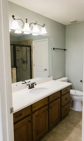 Bathroom vanity featuring a single basin sink, white countertop, and wood-finish cabinetry with dark hardware