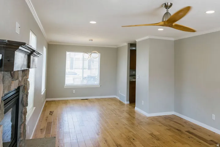 Spacious interior featuring wide-plank wood flooring, a stone-clad fireplace with a dark wood mantel, and crown molding