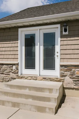 Double French doors with integrated blinds, stone veneer accents, shake siding, and a shingled roof