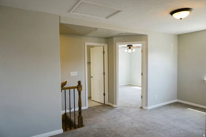 Carpeted upper-level space featuring a staircase with wood newel post and wrought iron balusters