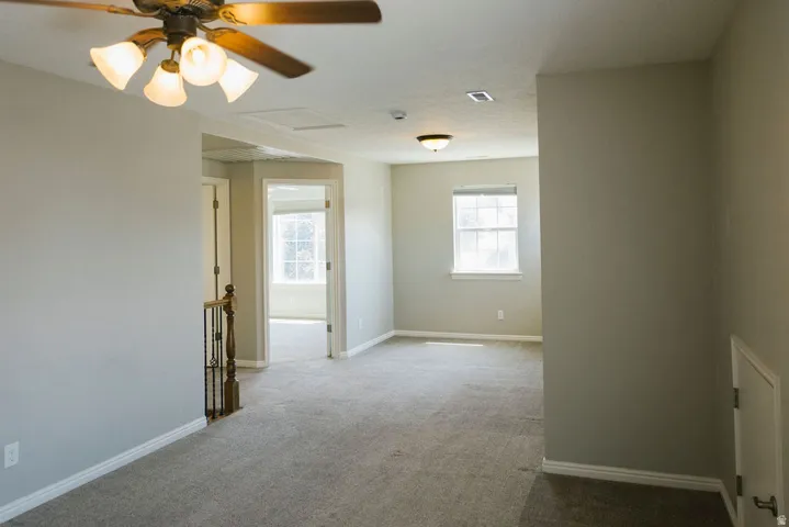 Spacious carpeted room featuring a ceiling fan with integrated lighting, a window with a roller shade, and light-colored walls