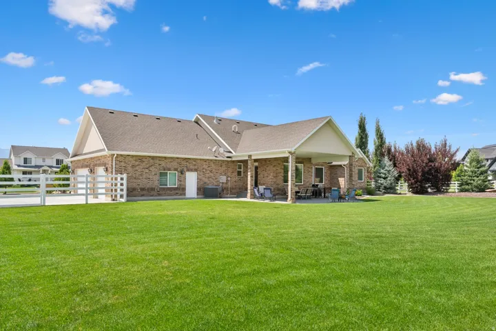 Expansive green lawn with a brick exterior home featuring a covered patio, attached garage, and white fencing