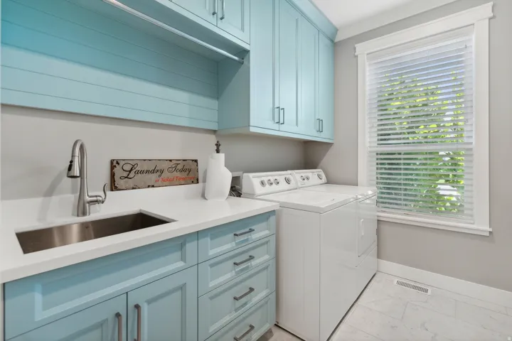 Laundry room featuring light blue cabinetry, a stainless steel sink with a high-arc faucet, and white countertops