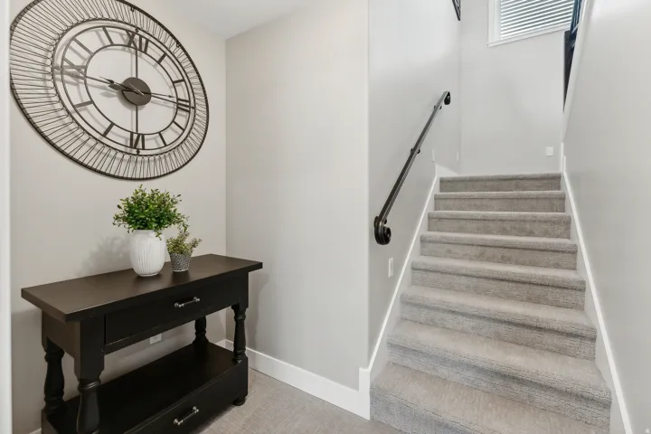 Carpeted staircase with a black metal handrail, light gray wall paint, white trim, and a built-in console table with storage