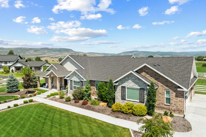 Brick and stone exterior featuring a covered entry, gabled rooflines, a manicured lawn, and mature landscaping