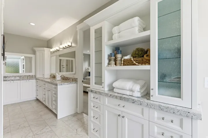Double vanity with dual undermount sinks, stone countertops, white cabinetry, and wall-mounted lighting