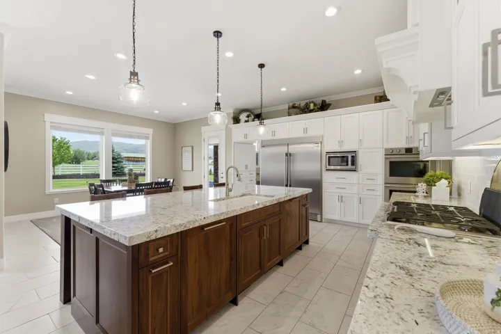 Gourmet kitchen featuring a large island with a natural stone countertop, stainless steel appliances, white cabinetry, recessed lighting, and tile flooring