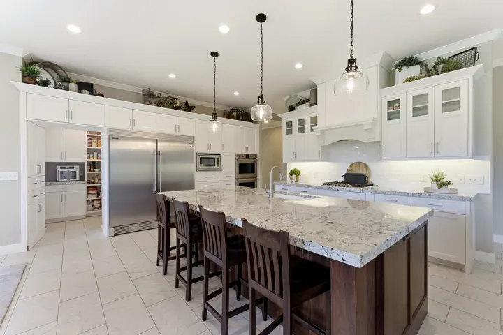 Spacious kitchen featuring an expansive island with a light-toned countertop, white cabinetry with crown molding, stainless steel appliances, pendant lighting, and ceramic tile flooring