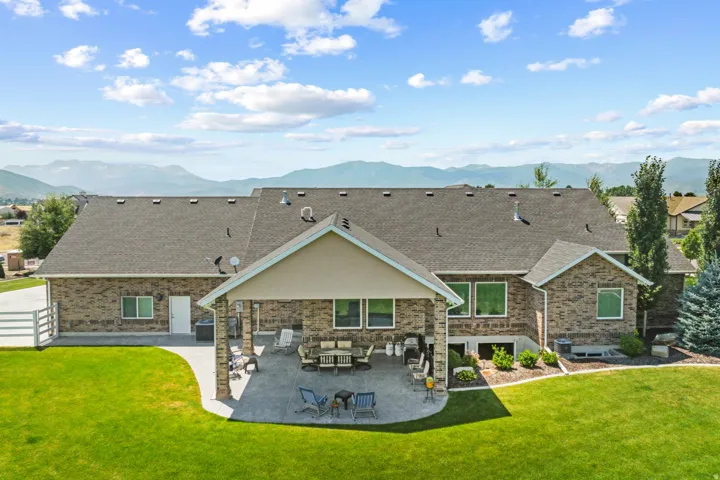 Spacious brick exterior home featuring a covered patio, expansive lawn, and a mountain backdrop