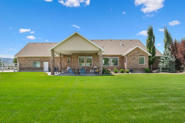 Expansive rear yard featuring a large green lawn, a covered patio with a concrete surface, and a brick exterior with multiple windows