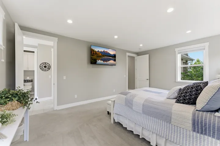Spacious bedroom featuring light gray walls, plush carpeting, recessed lighting, and a prominent window with white trim
