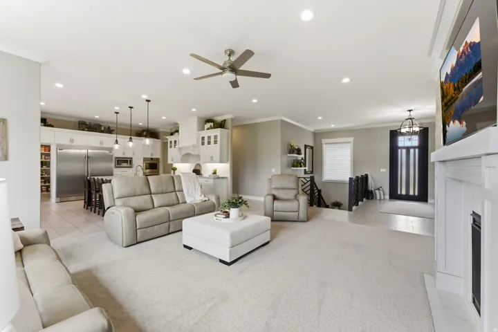 Open-concept living space featuring light-colored carpet flooring, a ceiling fan with integrated lighting, and recessed ceiling lights