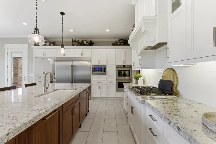 Gourmet kitchen featuring a large central island with an undermount sink, granite countertops, stainless steel appliances, a white tile backsplash, and a decorative range hood