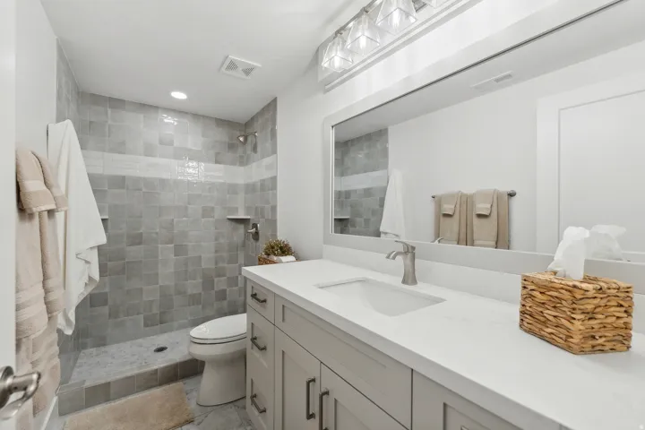 Shower with square grey wall tiling and an accent band of light grey horizontal tiles, featuring a built-in shower niche and a handheld showerhead