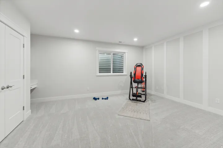 Spacious room featuring light gray carpeting, recessed ceiling lighting, a built-in window with horizontal blinds, and accent wall paneling