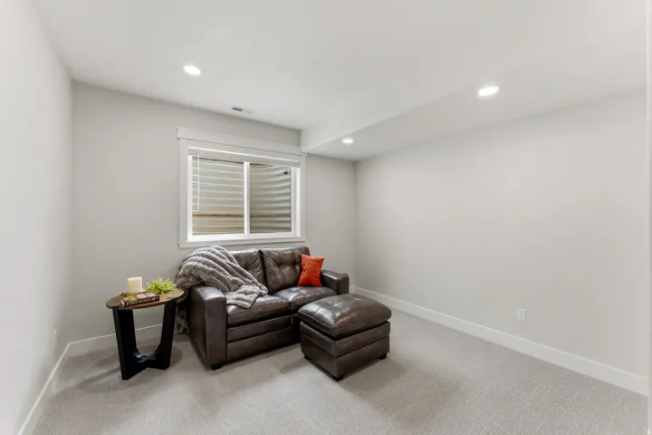 Recessed lighting illuminates this bright room featuring a window with blinds, light gray walls, white baseboards, and light-toned carpet flooring