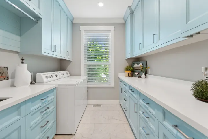Spacious laundry room featuring light blue cabinetry, white countertops, built-in shelving, and light-toned tile flooring