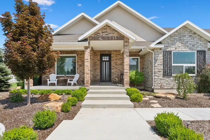 Exterior featuring a brick and stone facade, covered porch, concrete walkway, and established landscaping