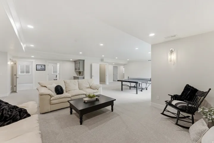 Spacious lower-level area featuring recessed lighting, light-colored carpeting, a built-in wet bar with glass-front cabinetry, and shaker-style doors